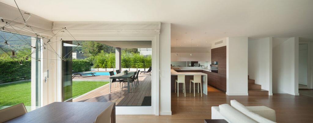 Luxuriöses Wohninterieur, großer offener Raum, Veranda und Blick aus den Fenstern auf den Garten mit Pool.