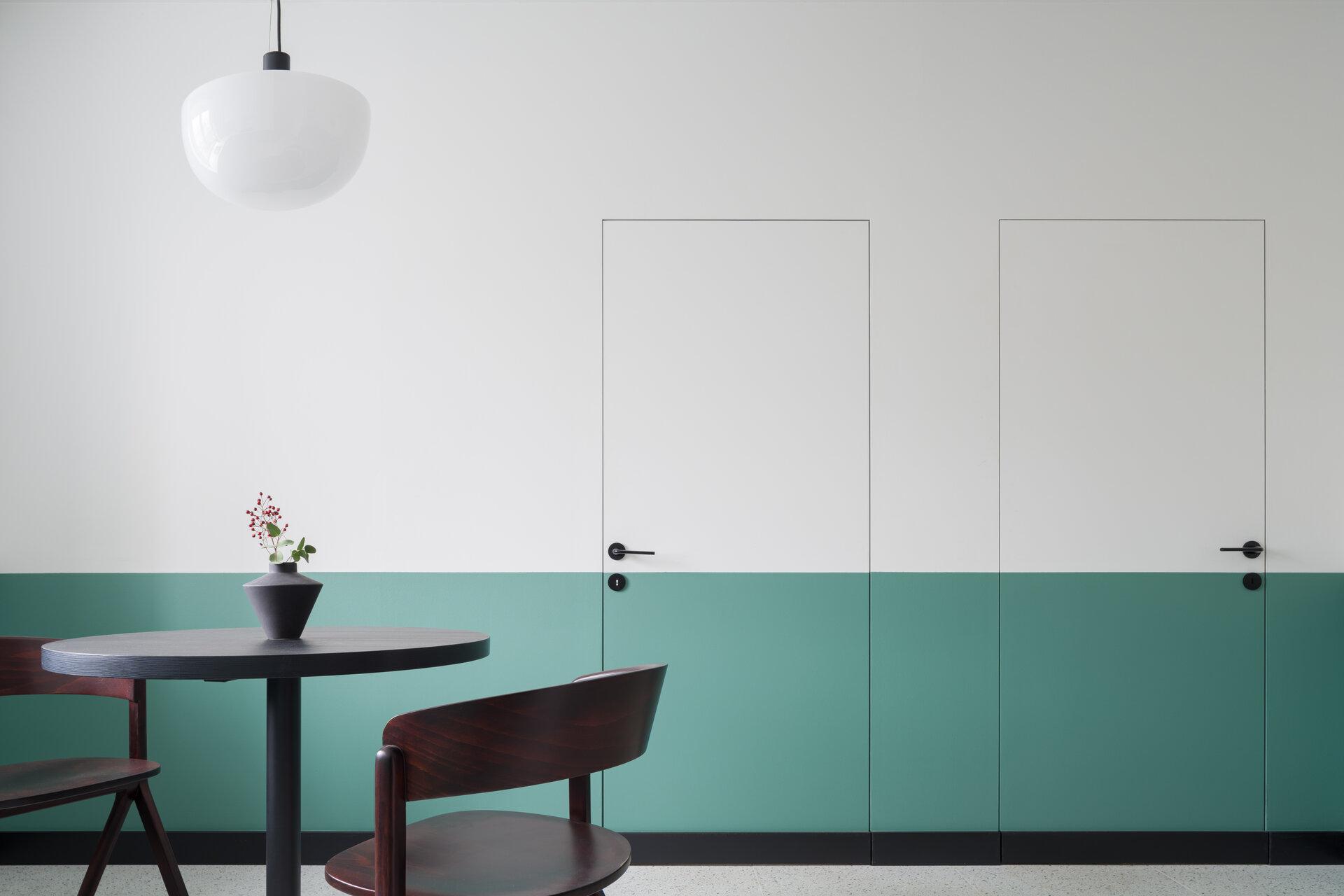 Modernes Architekturdesign mit halb grünen und weißen Türen und Wänden in einem stilvollen Esszimmer mit dunklem Tisch und Stühlen unter einer neuen Lampe