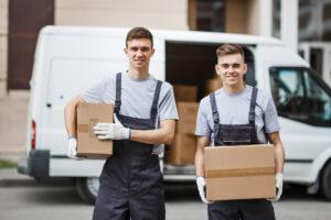 Zwei lächelnde Arbeiter in Uniform stehen vor einem Transporter voller Kisten und halten Kisten in den Händen.