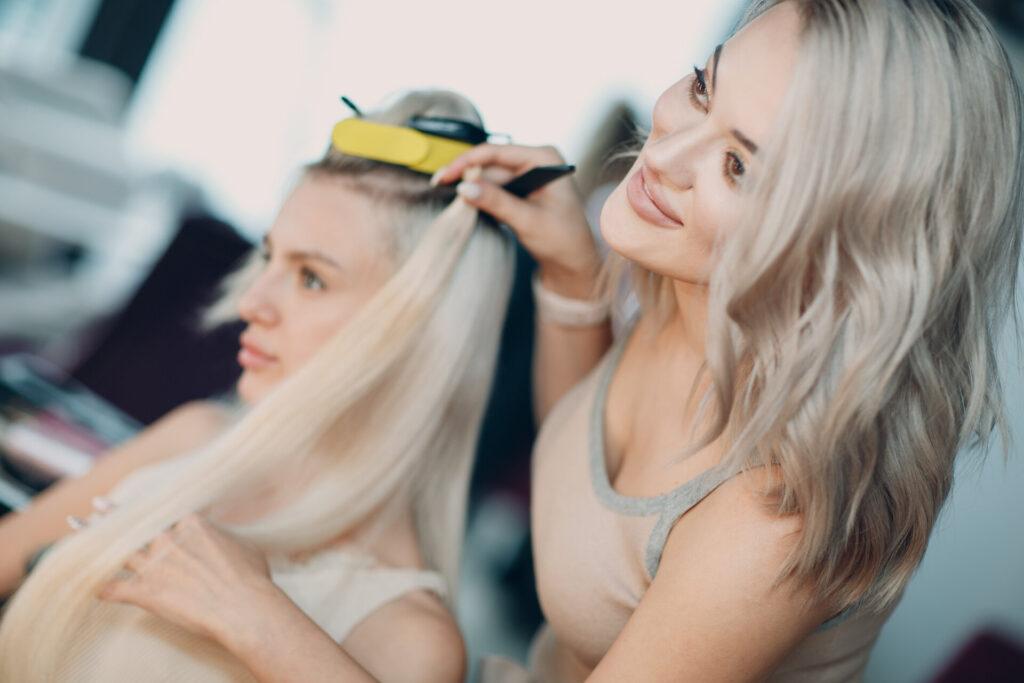 Friseurin macht Haarverlängerungen für junge Frau mit blondem Haar in Schönheitssalon. Professionelle Haarverlängerung.