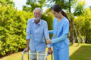 Junge asiatische Frau, Pflegerin, Krankenschwester, Betreuerin hilft älterem alten Mann mit Mobilität im Garten zu Hause.