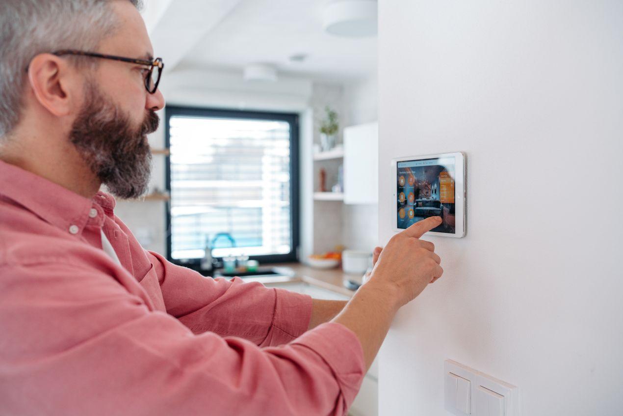 Mann steuert Smart-Home-System über Wand-Tablet beim Wohnzimmer gestalten