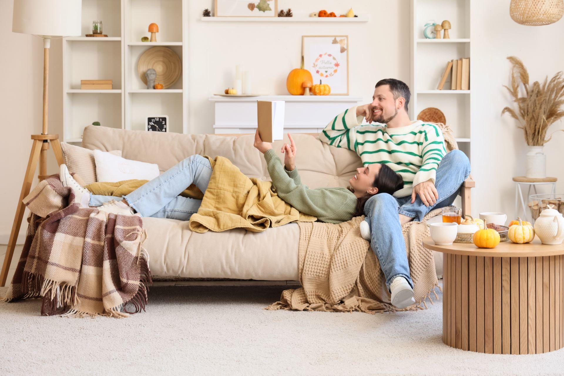 Paar liegt entspannt mit Decke auf Couch im hellen Wohnzimmer