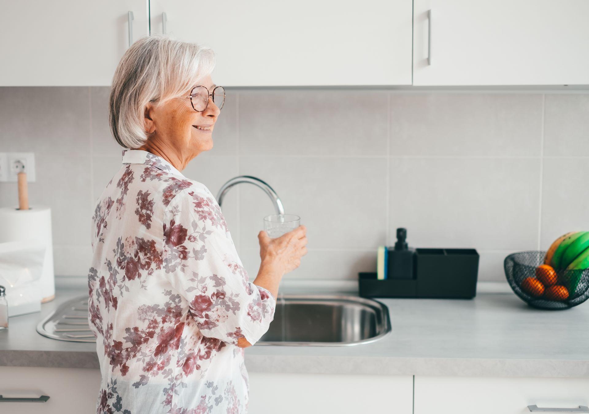 Seniorin freut sich über gespartes Wasser am Wasserhahn